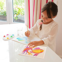 Load image into Gallery viewer, A child paints (or maybe just moves the brush) a fish on a kitchen table.  Shows the palette, which included five colors (blue, green, yellow, red, and pink). 
