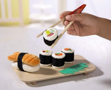 Load image into Gallery viewer, Set outside of packaging, a small hand uses the chop sticks to pick up a rice roll
