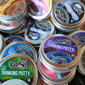 Image shows a variety of the Aaron's travel sized putty options in a pile together including an orange, blue, and silver option.   When ordering online we'll choose one for you!