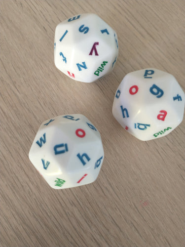 Three of the alphabet dice rolled onto a pale, laminate wood table. 
