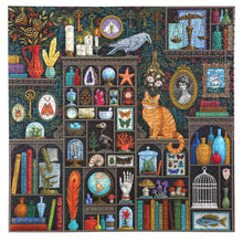Load image into Gallery viewer, Puzzle features curio cabinets and carved shelves set against dark damask wallpaper, highlight paintings in ornate frames, cloches, skeleton keys.  Dried flowers, framed flora and fauna also adorn the shelves.  Amongst the collection is a living orange cat staring out at the puzzle solver. Illustrated by Vasilisa Romanenko.
