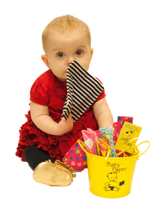 Image of a baby playing with Baby Paper, next to a bucket of more Baby Paper.  The Baby Paper is about the size of the child's head.  